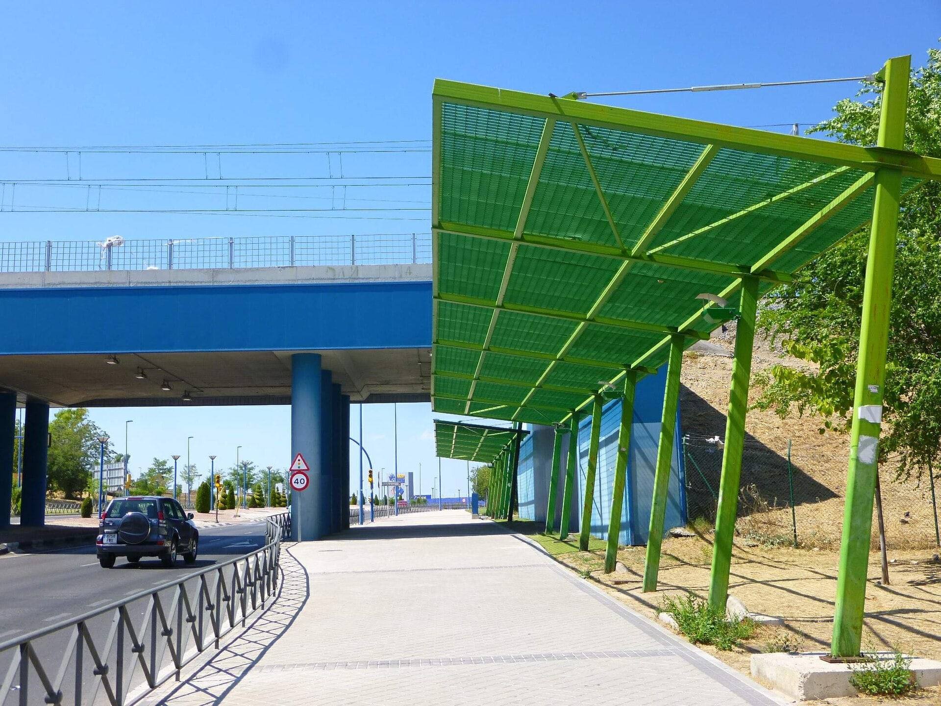 Acceso peatonal a Leganés Norte bajo una pérgola verde, junto a un paso elevado